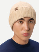 Person wearing a beige knit beanie with a logo on a white background