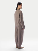 A model shown from the back wearing a matching taupe knit mock-neck sweater and wide-leg trousers set, paired with flat taupe shoes, against a plain light gray background.