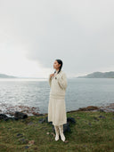 A woman wearing a beige knit cashmere skirt with an elasticated high-waist, paired with a white blouse with a sleeve detail.  #color_off-white