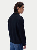 A man shown from the back wearing a dark navy knit sweater and blue jeans, photographed against a clean light gray studio background.