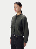 A model wearing a dark olive green cropped knit cardigan with braided trim details, paired with black jeans, against a light gray studio background.