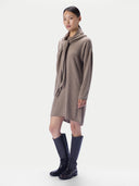 A model wearing a taupe knit cowl-neck sweater dress with a matching knit scarf, paired with black knee-high leather boots, against a plain light gray studio background.