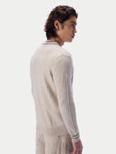 A man shown from the back and side wearing a ribbed knit sweater in a light cream or oatmeal color, paired with matching light pants, against a plain light gray studio background.