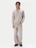 A man modeling a light beige knit quarter-zip pullover sweater and matching wide-leg trousers against a plain light gray studio background.