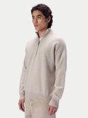 A man wearing a light beige quarter-zip knit sweater and matching trousers, photographed against a clean light gray studio background.