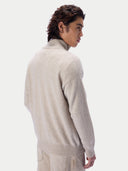 A man wearing a light beige knit mock-neck sweater, shown from a three-quarters back view against a plain light gray studio background.