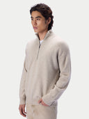 A man wearing a light beige knit quarter-zip sweater and matching trousers, photographed against a clean light gray studio background.