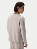A man shown from the back wearing a light beige knit sweater and matching trousers against a plain light gray studio background.