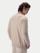 A man wearing a light beige knit sweater, shown from a rear three-quarter angle against a plain light gray studio background.