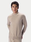 A man wearing a light beige knit mock-neck sweater, photographed against a clean light gray studio background.