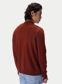 A man wearing a rust-brown knit sweater with a mock neck, shown from a three-quarters back view against a light gray studio background.