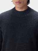 Close-up of a person wearing a dark charcoal gray knit sweater with a ribbed crew neck, shown against a plain light background.