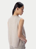 A model shown from the back wearing a light beige sleeveless knit top and matching trousers against a plain light gray studio background.