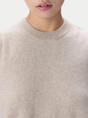 Close-up of a person wearing a soft knit crew-neck sweater in a light warm beige color, against a plain light background.