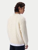 A man wearing a cream-colored cable-knit sweater, shown from a three-quarters back view against a light gray studio background.