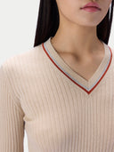 Close-up of a model wearing a ribbed cream V-neck sweater with thin red and light blue striped trim along the neckline.