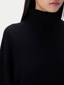 Close-up of a person wearing a black ribbed turtleneck sweater against a light gray background.