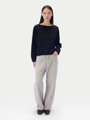 A woman modeling a black long-sleeve boat-neck knit top and light beige wide-leg trousers against a plain white studio background.