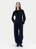 A model stands against a light gray studio background wearing a matching black knit top and wide-leg pants set, paired with black shoes.