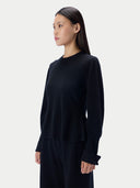 A woman modeling a black long-sleeve crewneck top and matching black pants against a light gray studio background.