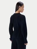 A model shown from the back wearing a black long-sleeve crewneck top and matching black pants against a light gray studio background.