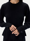 A model shown from the back wearing a black long-sleeve crewneck top and matching black pants against a light gray studio background.