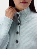 Close-up of a person wearing a ribbed knit mock-neck sweater in a pale icy blue color, with dark buttons down the front.