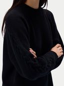 A close-up of a person wearing a black knit sweater with textured cable detailing on the sleeves, shown against a plain light background.