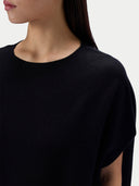 Close-up of a model wearing a black short-sleeve knit top against a light gray background.