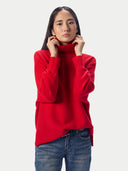A woman wearing a bright red knit turtleneck sweater and blue jeans, posing against a light gray studio background.