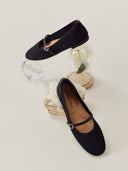 Pair of black flat shoes with a strap on a light gray background #color_black