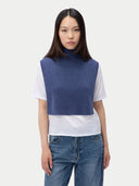 Person wearing a blue knitted vest over a white shirt with blue jeans on a white background. #color_soft-indigo