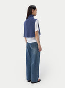 Person wearing a blue vest over a white shirt and blue jeans on a white background. #color_soft-indigo
