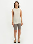 A woman wearing a sleeveless beige knitted top with a round neckline . #color_white