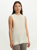 A woman wearing a sleeveless beige knitted top with a round neckline . #color_white