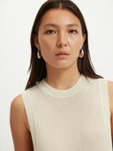 A woman wearing a sleeveless beige knitted top with a round neckline . #color_white