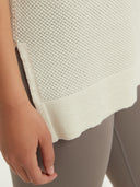 A woman wearing a sleeveless beige knitted top with a round neckline . #color_white
