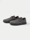 A pair of low-top sneakers in dark gray and black, featuring a textured fabric upper, matching gray laces, and black soles, photographed on a light gray studio background. #color_cool-stone