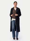 Black coat worn unbelted over a brown V-neck sweater, white tee and jeans