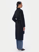 Back view of the black long coat showing belt tie and straight silhouette