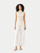 Woman wearing a cream sleeveless top and white pants on a light gray background #color_cream-white