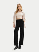 Woman wearing a beige top, light pink cardigan, black pants, and black boots on a white background #color_off-white