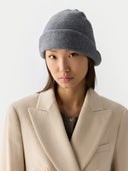 Person wearing a gray knit beanie and beige coat on a white background