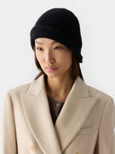 Woman wearing a black beanie and a beige coat against a white background