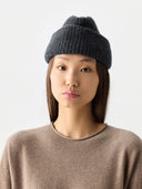 Woman wearing a dark gray knit beanie on a light gray background