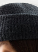 Woman wearing a dark gray knit beanie on a light gray background