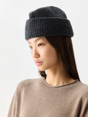 Woman wearing a dark gray knit beanie on a light gray background