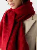 close up of a person wearing a red scarf and beige coat against a neutral background