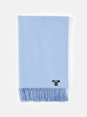 A light blue knit scarf with fringe detailing and a small black GARM brand tag near the bottom right, displayed flat against a solid white background.
