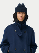 Person wearing a blue coat and matching beanie on a white background